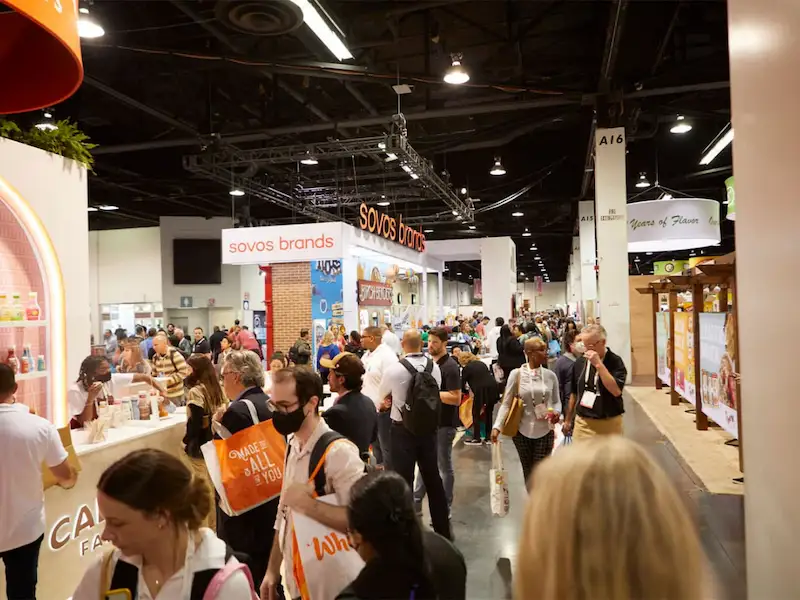 Attendees walking a busy trade show aisle lined with exhibitor booths