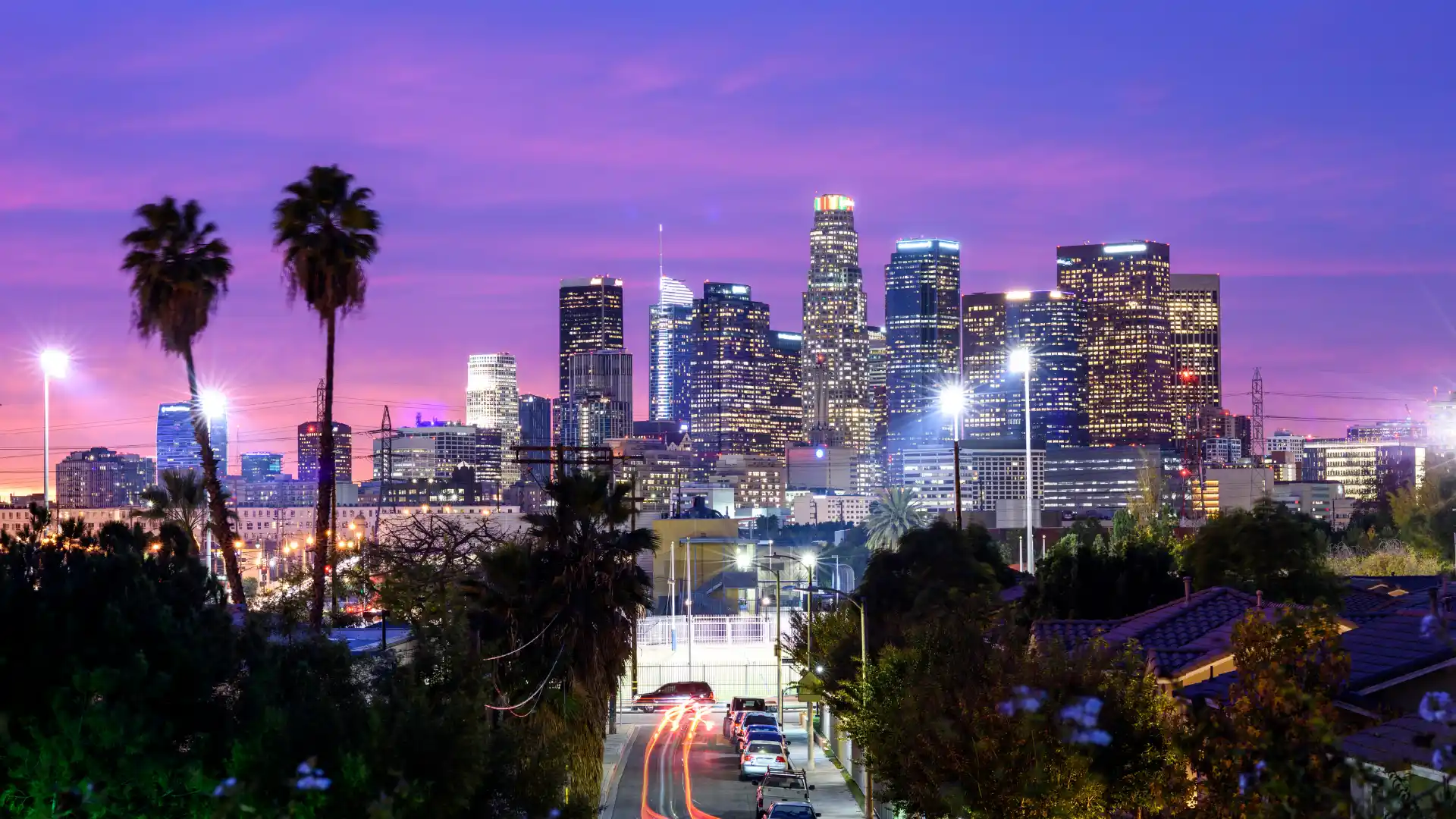 Los Angeles skyline at dusk with illuminated downtown buildings and palm trees