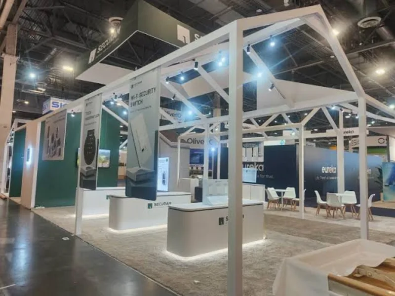 An open-sided custom exhibit stand with an overhead frame on a show floor