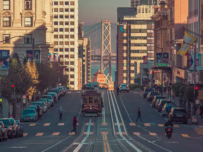 A cable car climbing a San Francisco street with the Bay Bridge in the distance